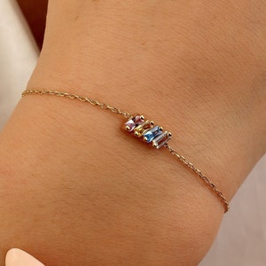 May include: A gold chain bracelet with a small cluster of colorful gemstones.