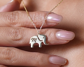 Può includere: Una collana con catena dorata e un piccolo ciondolo a forma di elefante in argento. L'elefante ha la lettera "M" incisa sul fianco.
