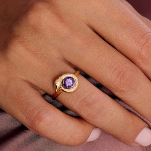 May include: A gold ring with a purple gemstone set in a textured, snake-like design.