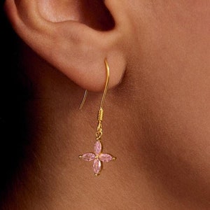May include: Gold dangle earrings with a pink flower design.