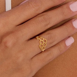 May include: A gold honeycomb ring with a delicate design. The ring is worn on the finger of a person with light skin.