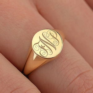 May include: A gold signet ring with a round oval top featuring a monogrammed design.