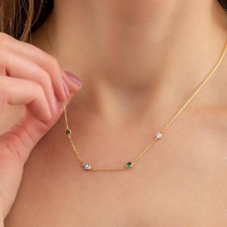 May include: A gold chain necklace with four small gemstones: green, blue, clear, and green.