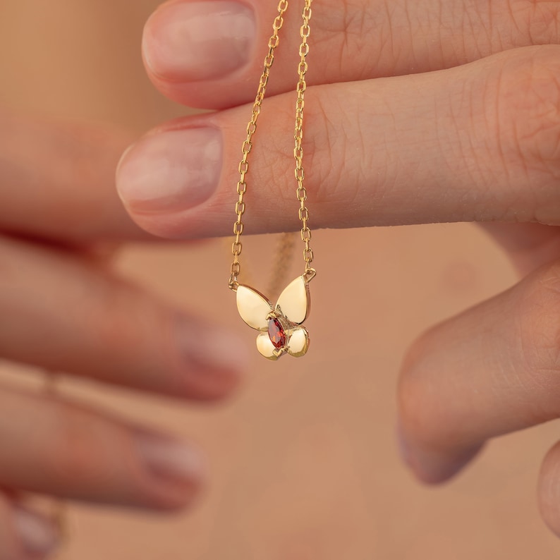 May include: A gold chain necklace with a butterfly pendant featuring a red gemstone.
