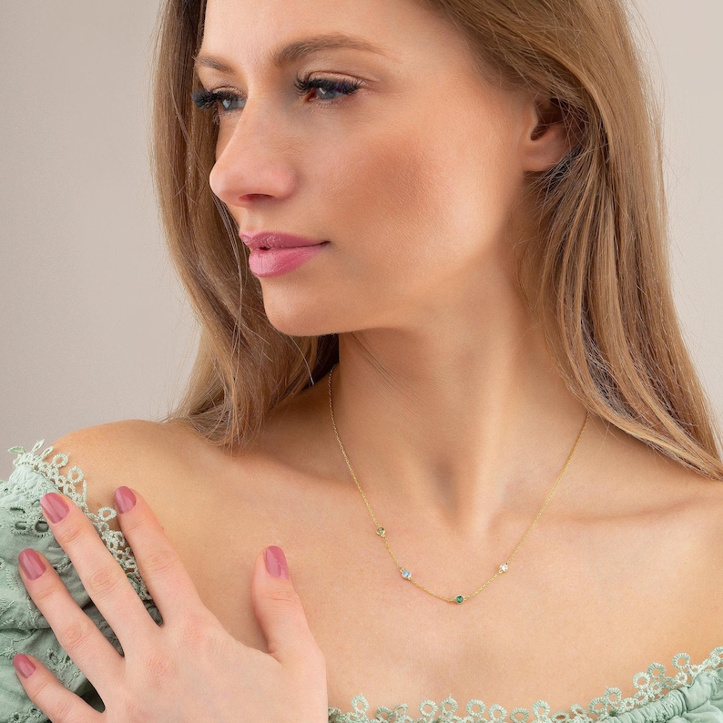 May include: A gold chain necklace with small green and white gemstones. The necklace is worn by a person with long blonde hair.