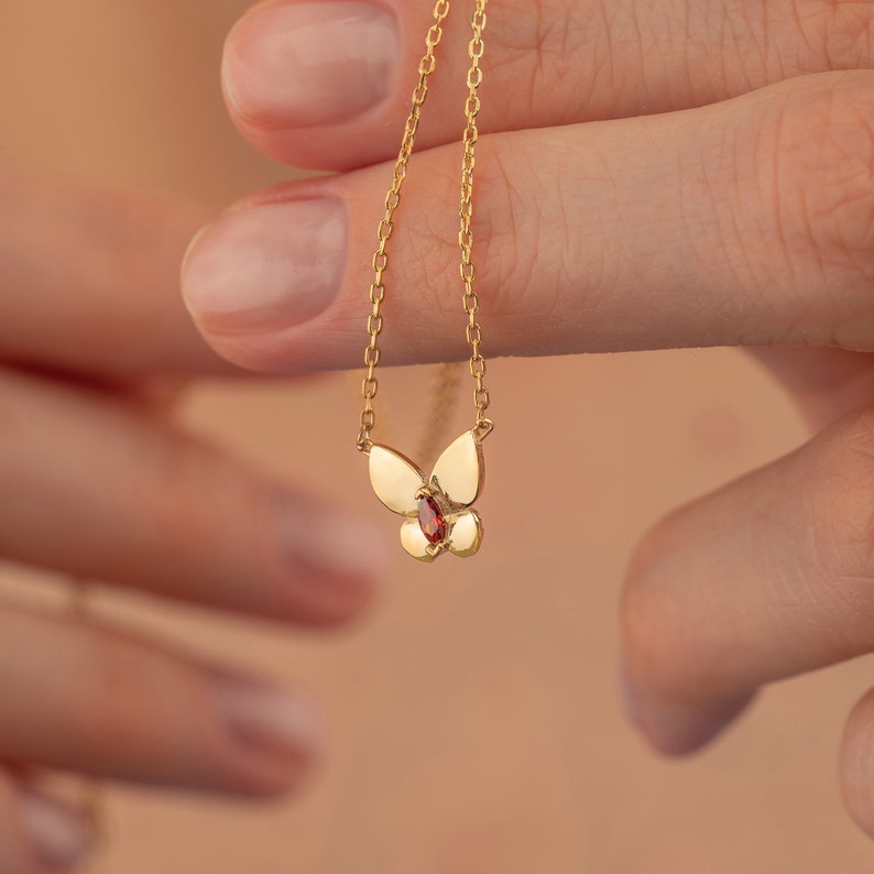 May include: A gold chain necklace with a butterfly pendant featuring a red gemstone.