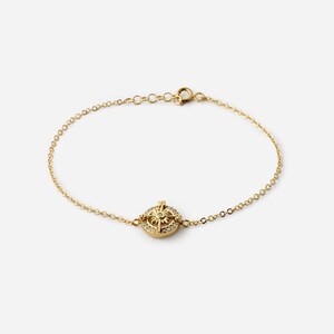 May include: A delicate gold-colored bracelet featuring a circular pendant with a compass design. The pendant is encrusted with small, clear gemstones. The bracelet has a fine chain and a clasp closure. The jewelry is set against a plain background.