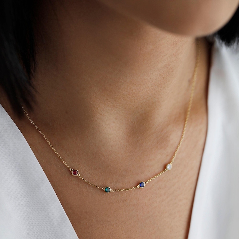 May include: A gold chain necklace with four small round gemstones: red, green, blue, and white.
