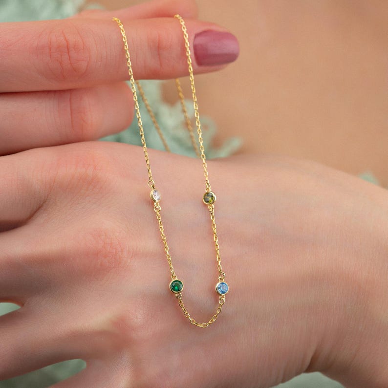 May include: A gold chain necklace with four small gemstones. The gemstones are clear, green, blue, and yellow.