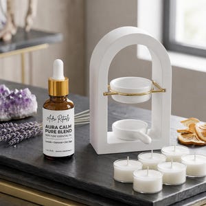 May include: A brown glass essential oil bottle labeled Adri Rituals Aura Calm Pure Blend 1 fl oz 30 ml, a white arched oil burner with a gold metal ring, and six white tea light candles. The bottle lists Lavender, Chamomile, and Clary Sage.