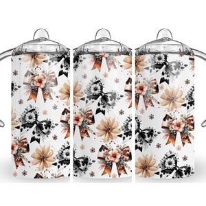 May include: Three white mugs with a black and white cow print bow design and floral accents. The mugs have clear lids and handles.