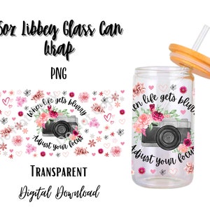 以下が含まれることがあります： 473 ml のガラス缶のラッピングで、花柄のデザインと「When life gets blurry, adjust your focus」というテキストが書かれています。デザインにはカメラ、ピンクの花、ハートが描かれています。