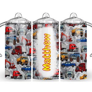 May include: A white tumbler with a clear lid and a handle. The tumbler has a colorful pattern of trucks, diggers, and cars. The name "Matthew" is printed on the tumbler.