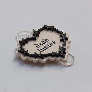 May include: A white heart-shaped charm with a black barbed wire border and the text "dead inside" in black.
