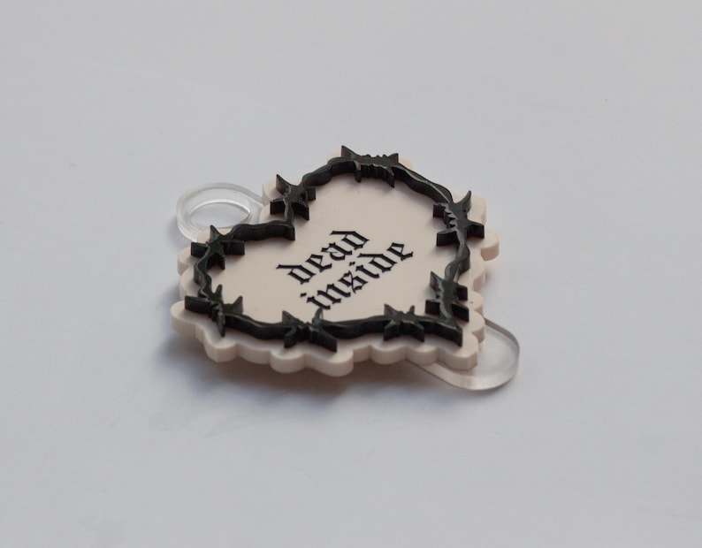 May include: A white heart-shaped charm with a black barbed wire border and the text "dead inside" in black.