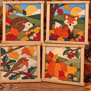May include: Four square fabric wall hangings in light wooden frames featuring autumn scenes: a hedgehog, a fox, a robin on a branch, and pumpkins. Each piece displays quilted fabric patches in seasonal colours like orange, red, and brown.