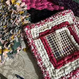 May include: A close-up of a red and white rug with a mesh centre. The rug is made of fabric strips and is being worked on with a red needle and yarn.