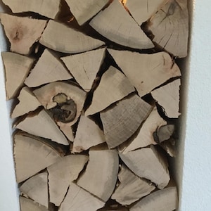 Può includere: Un primo piano di una pila di legna da ardere, disposte in un motivo decorativo. Il legno è di colore marrone chiaro e ha un aspetto naturale e rustico.