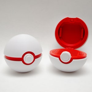 May include: A white and red Poke Ball toy with a red button on the front. The toy is open to reveal a red interior with a grid pattern.