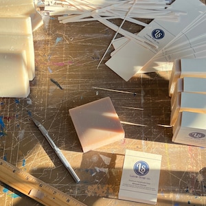 Może przedstawiać: Drewniana linijka, srebrny nóż uniwersalny i kostka ręcznie robionego mydła na drewnianej powierzchni. Mydło jest oznaczone "Lucas Soap Co. Premium Handmade Soap Almond Coconut".