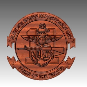 May include: A wooden emblem featuring the words "ELEVENTH MARINE EXPEDITIONARY UNIT" and "PRIDE OF THE PACIFIC". The emblem includes an eagle, globe, anchor, and a rifle. The design is carved into the wood.
