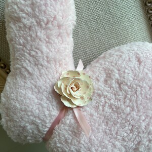 May include: A pink fluffy bunny rabbit with a white and pink polka dot flower and a pink ribbon.