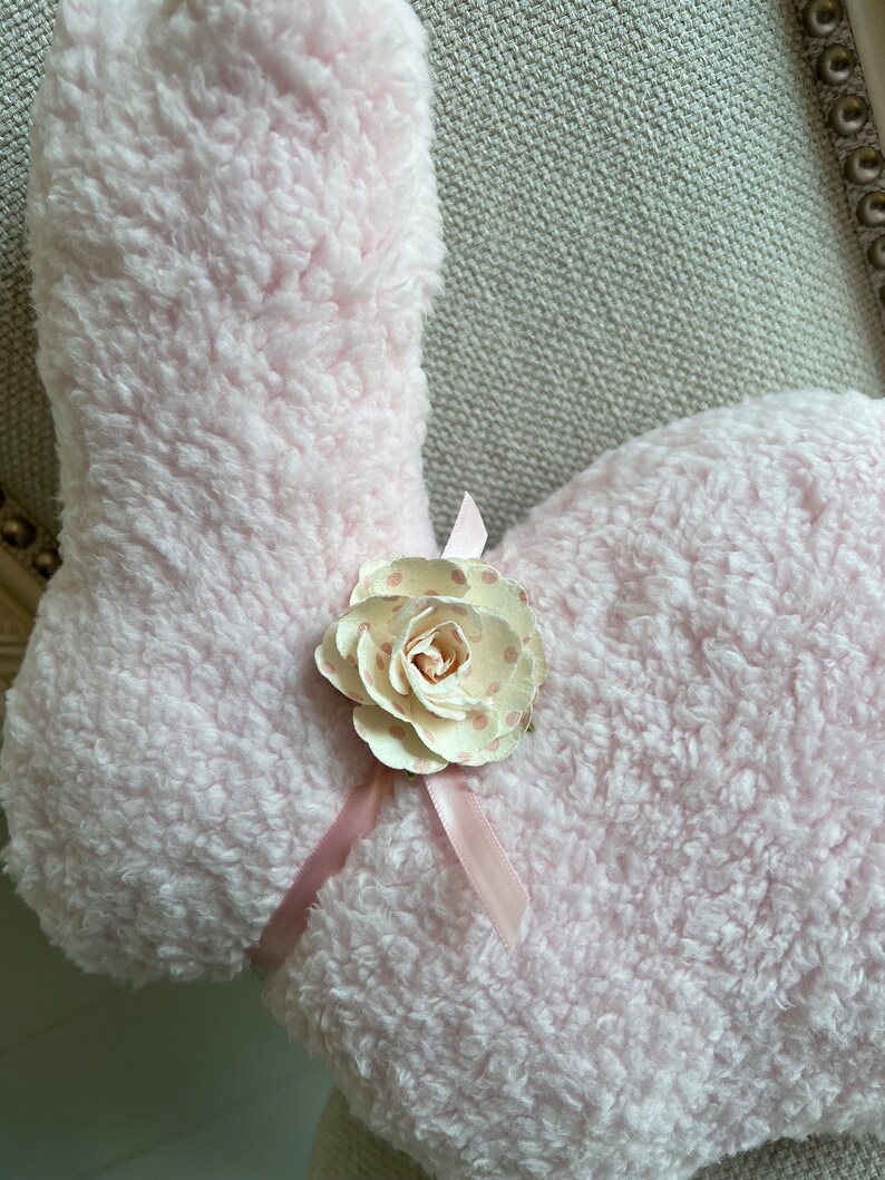 May include: A pink fluffy bunny rabbit with a white and pink polka dot flower and a pink ribbon.