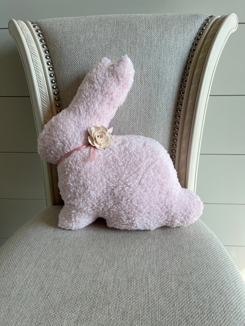 May include: A pink plush bunny rabbit pillow with a pink flower accent on a light gray chair.