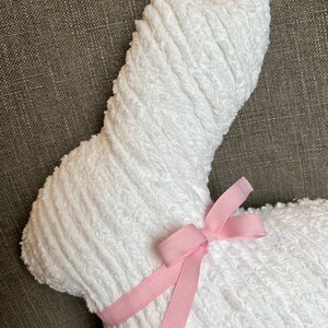 K&ouml;nnte beinhalten: Ein wei&szlig;er Pl&uuml;schhase mit einem rosa Band um den Hals. Der Hase ist aus einem weichen, strukturierten Stoff.