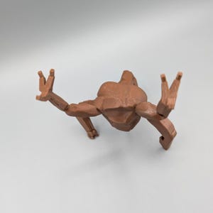 May include: A brown, articulated figure in a crawling pose, with arms and legs extended. The figure has a geometric, blocky design, with visible joints. The figure is positioned against a plain, light background.