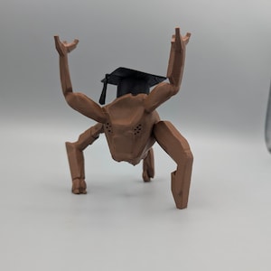May include: A brown, stylized, four-legged creature with raised arms and a black graduation cap. The figure has a textured surface and is posed against a plain background, suggesting a whimsical or academic theme.