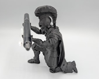 May include: A black 3D-printed figurine of a kneeling warrior wearing a crested helmet and armor, holding a black pen horizontally in both hands. The warrior is depicted in a defensive stance with a cape draped over the back and shoulders.