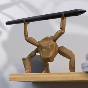 May include: A gold-colored pen holder in the shape of a stylized figure, holding a black pen. The pen holder is on a wooden shelf. The pen is black with a silver tip.