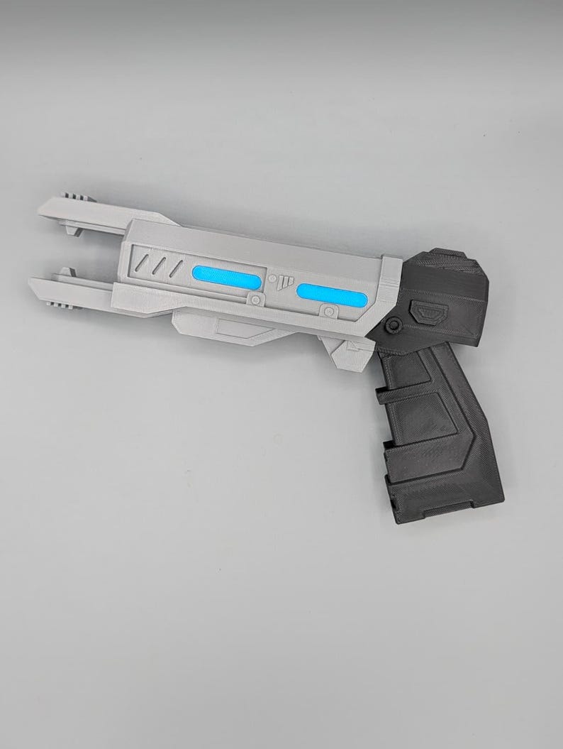 May include: A sci-fi style toy blaster featuring a light gray barrel with two horizontal bright blue accents and a dark gray handle. The barrel has a pronged front end and geometric detailing along the side, while the grip has a textured surface.