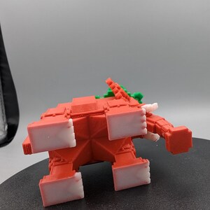 May include: A red, geometric elephant figurine with white accents on its feet and tusks. The elephant has a green and red design on its back. The toy is made of plastic and is sitting on a black surface.