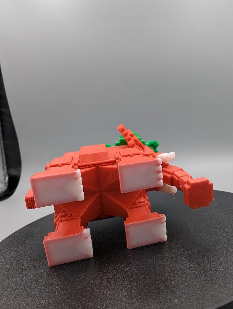 May include: A red, geometric elephant figurine with white accents on its feet and tusks. The elephant has a green and red design on its back. The toy is made of plastic and is sitting on a black surface.