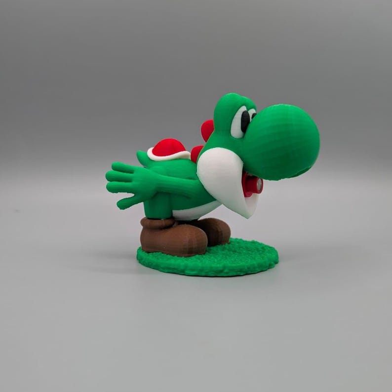Puede incluir: Una figura verde de Yoshi con caparaz&oacute;n rojo y botas marrones. La figura est&aacute; posada sobre una base de hierba verde, con boca blanca y lengua roja. El personaje es de la serie de videojuegos Super Mario.