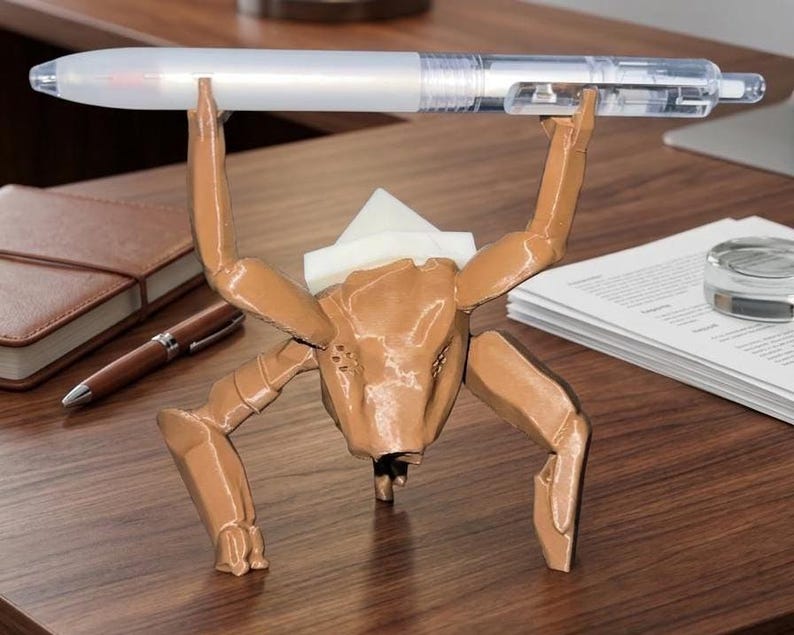 May include: A brown, insect-like pen holder with a pen held in its arms. The pen holder is made of a 3D-printed material and has a unique, artistic design. The pen is white and clear.