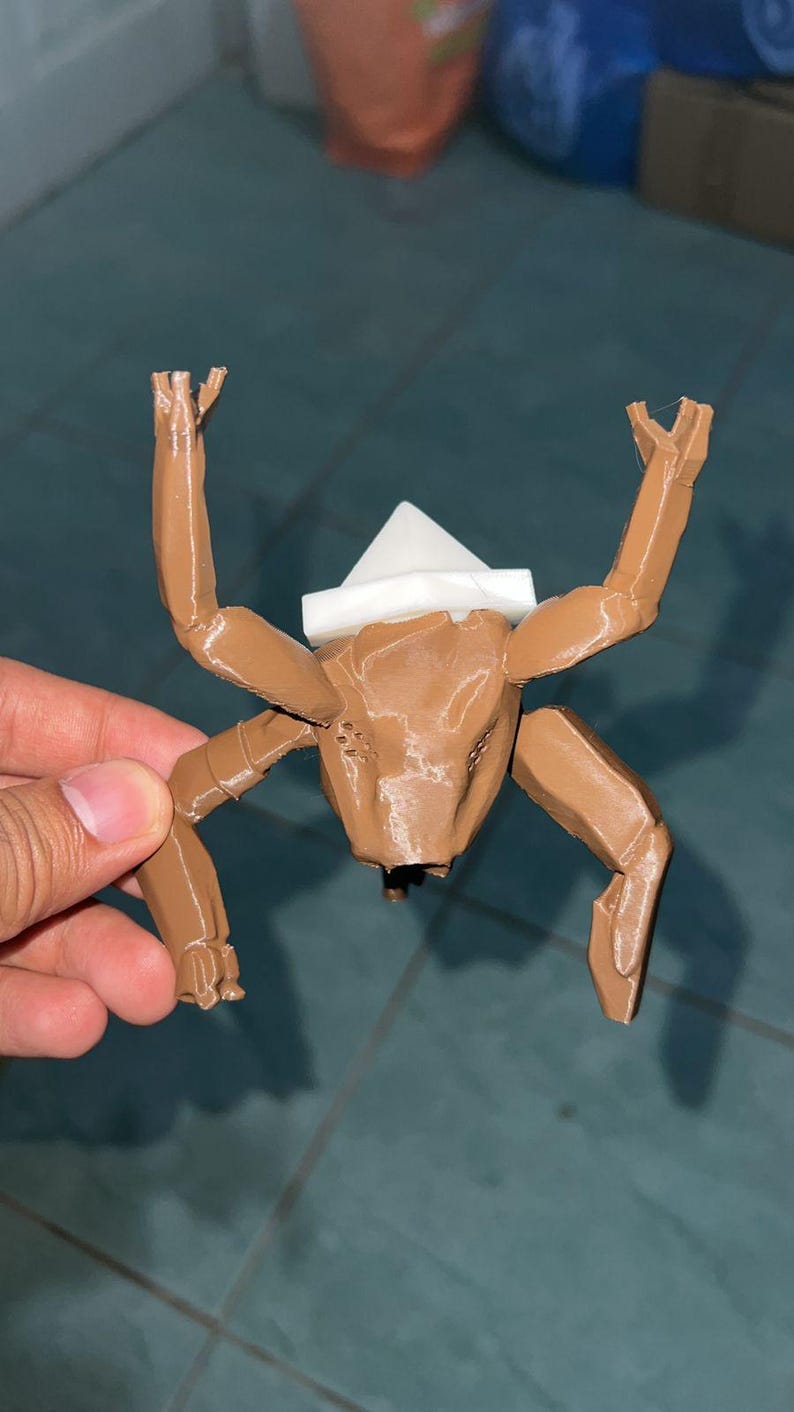 May include: A brown, 3D-printed insect-like figurine with a white headpiece. The figurine has multiple articulated limbs and a detailed, textured body. The arms are raised, and the legs are bent.