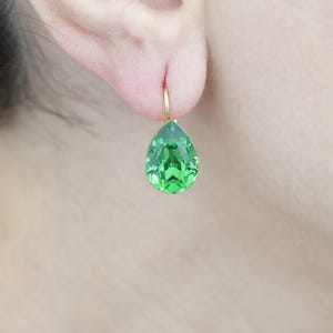 Puede incluir: Un par de pendientes de aro dorados con un cristal verde en forma de lágrima.
