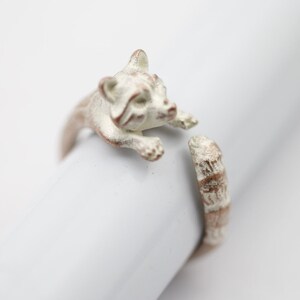 May include: A white metal ring with a raccoon design. The raccoon is curled up with its tail wrapped around the ring band.