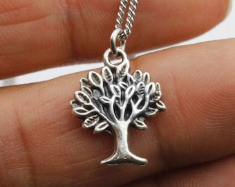 Puede incluir: Collar con colgante de árbol plateado. El colgante presenta un diseño detallado de árbol con hojas y ramas. La cadena del collar es de color plata delicado.