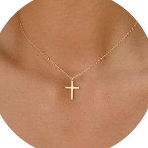 May include: A gold-coloured necklace with a small cross pendant. The cross hangs from a delicate chain. The necklace is shown against a skin-toned background.