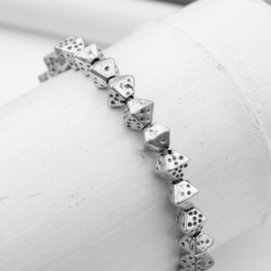 May include: A silver bracelet made of small, pyramid-shaped beads with a textured surface.