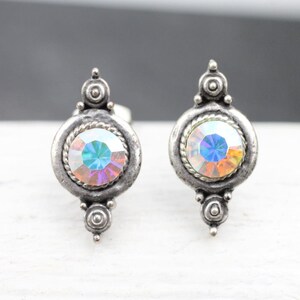 May include: A pair of silver earrings with iridescent round stones set in a decorative frame. Each earring has a small silver design at the top.