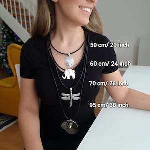 May include: Four layered black leather necklaces with silver pendants. The pendants are a spiral, an elephant, a dragonfly, and a circle. The necklaces are labeled with their lengths in inches and centimeters: 20 inches/50 cm, 24 inches/60 cm, 28 inches/70 cm, and 38 inches/95 cm.