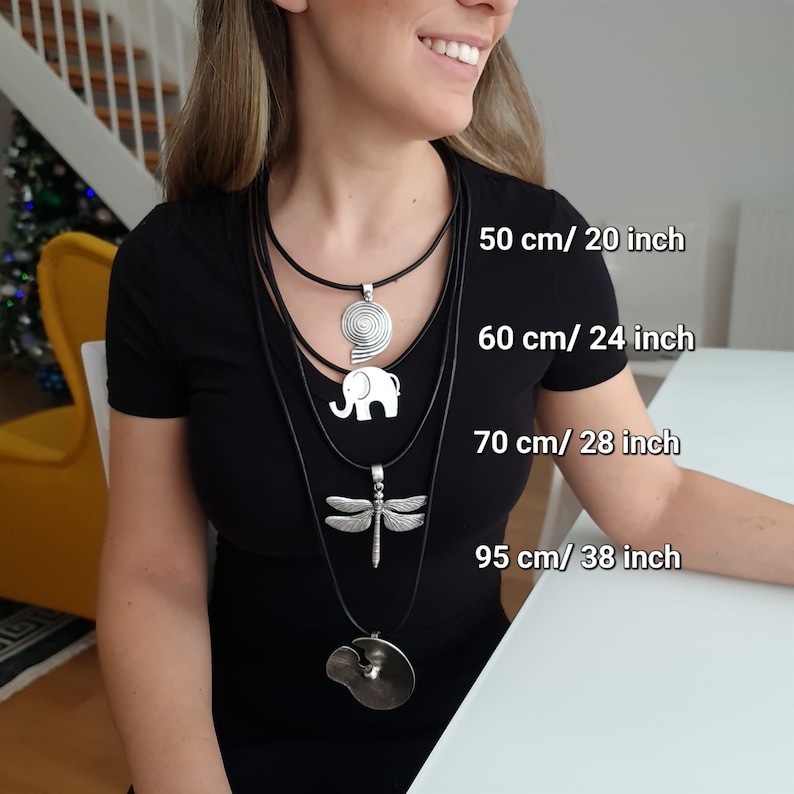 May include: Four layered black leather necklaces with silver pendants. The pendants are a spiral, an elephant, a dragonfly, and a circle. The necklaces are labeled with their lengths in inches and centimeters: 20 inches/50 cm, 24 inches/60 cm, 28 inches/70 cm, and 38 inches/95 cm.