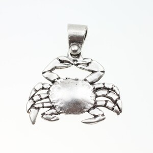 May include: A silver crab pendant charm with a detailed design. The charm has a loop at the top for attaching to a necklace or bracelet.