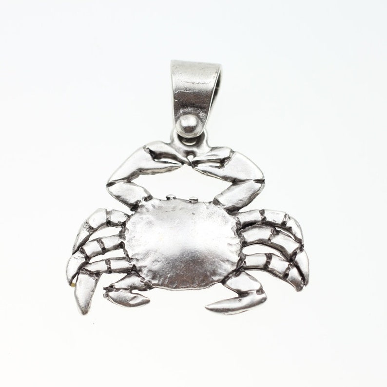 May include: A silver crab pendant charm with a detailed design. The charm has a loop at the top for attaching to a necklace or bracelet.