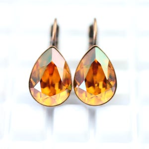 Puede incluir: Un par de pendientes en forma de lágrima con piedras de cristal de color ámbar y engastes de metal de color bronce antiguo.
